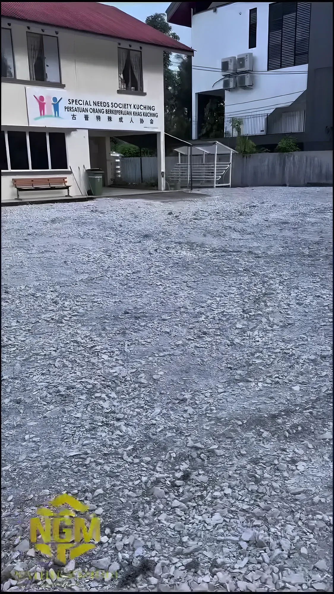 Finished gravel parking area in front of a community centre in Kuching, crusher run compacted level with the building behind.