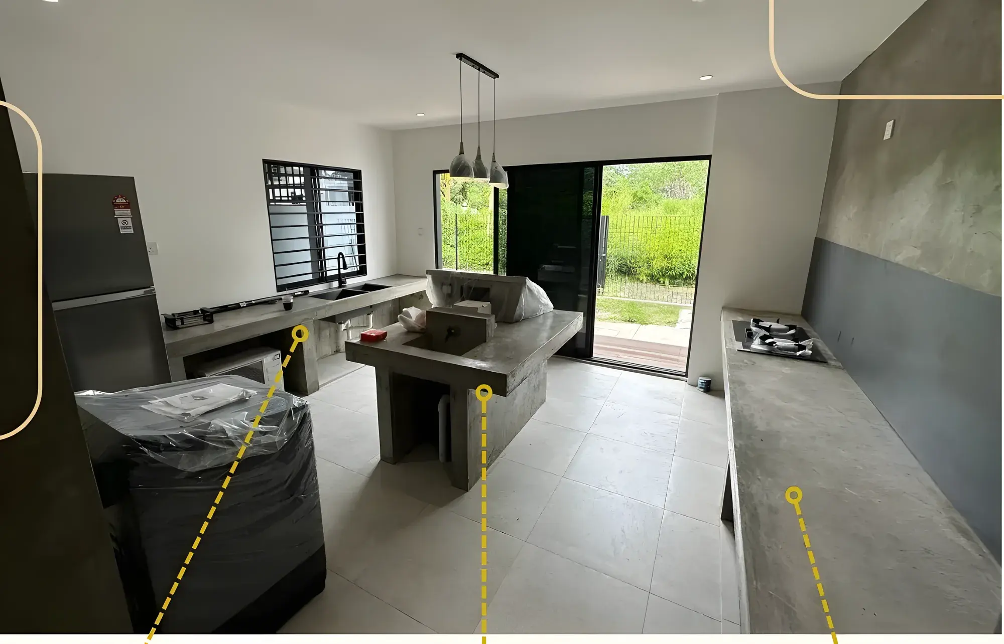 Kitchen with a cast concrete island, sink counter and worktop in cement finish, pendant lights and a window onto the garden.